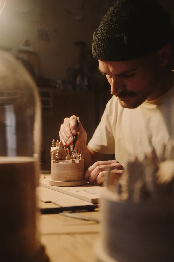 Thibaut Malet sculptant un univers miniature sous cloche en bois.